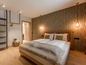 Wooden double bed with pendant lights and patterned wallpaper