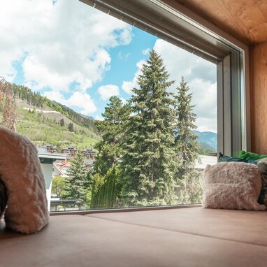 Cozy window seat indoors with mountains and trees outside.