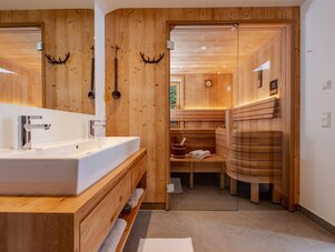 Bathroom area with twin sinks and wooden sauna beyond.