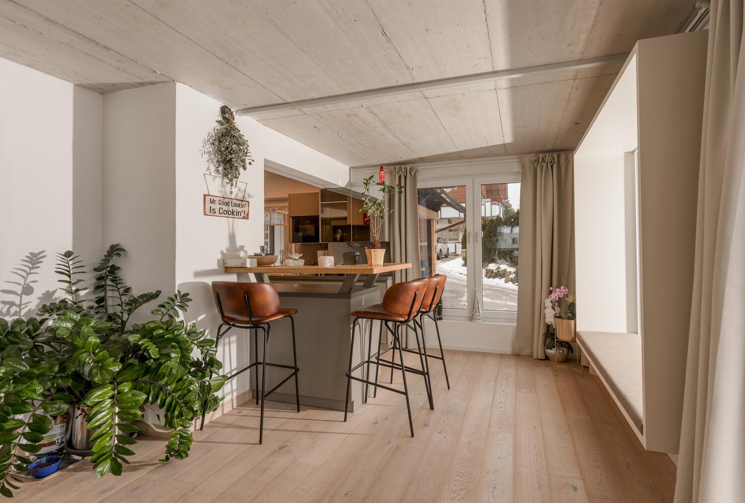 Moderner Küchenbereich mit Barhockern, Pflanzen und Vorhängen.