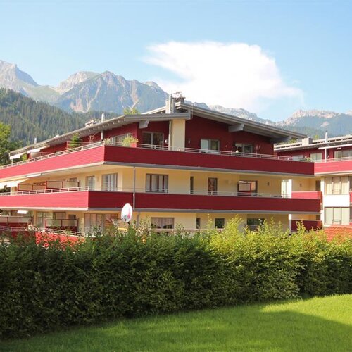 Red and cream apartment building with balconies, mountains in background