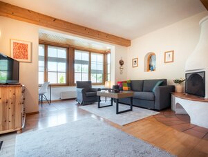 Gemütliches Wohnzimmer mit Sofa, Kamin und großen Fenstern | © TIEBER