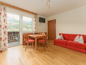 Wohnzimmer mit Holzboden, rotem Sofa und Esstisch