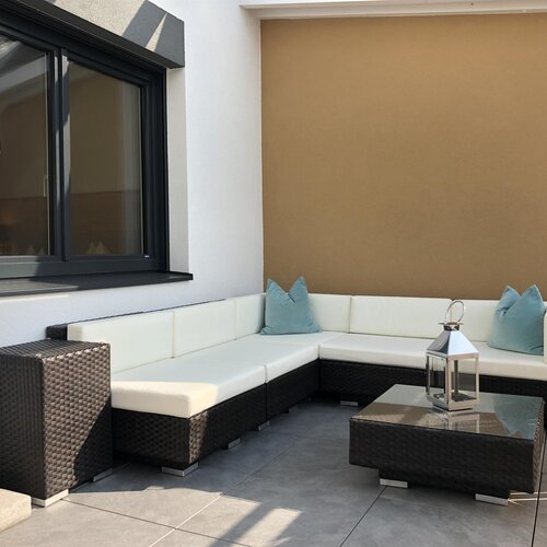 Witterungsfeste Rattan-Eckcouch mit weißen Polstern und blauen Kissen im Außenbereich