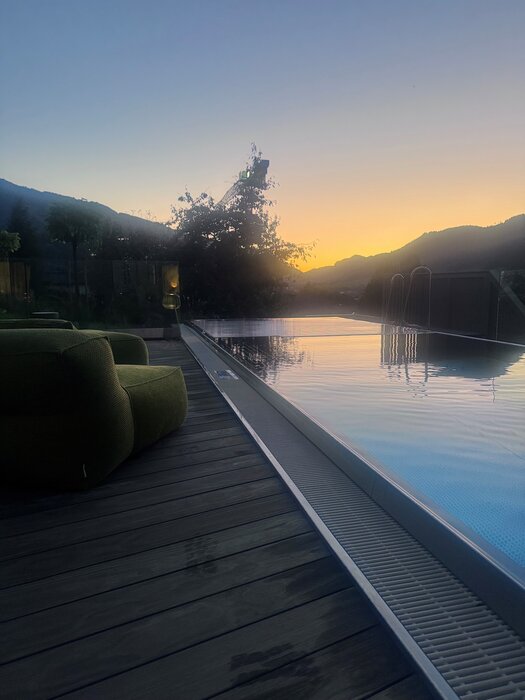 Infinity-Pool neben Holzdeck mit Sonnenuntergang im Hintergrund