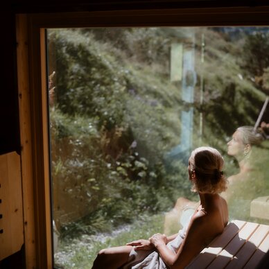 Frau im Saunaraum, in Handtuch gewickelt, blickt nach draußen