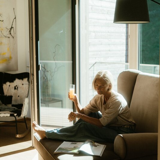 Older woman sits on a sofa near sliding door with drink