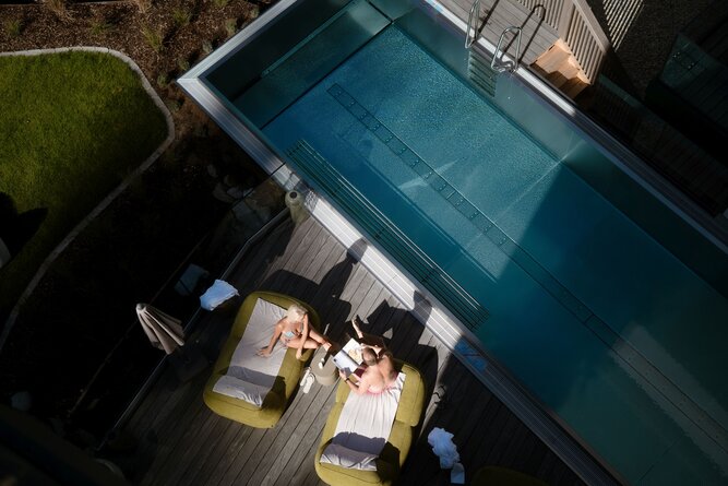 Zwei Personen entspannen sich auf grünen Liegen am Pool