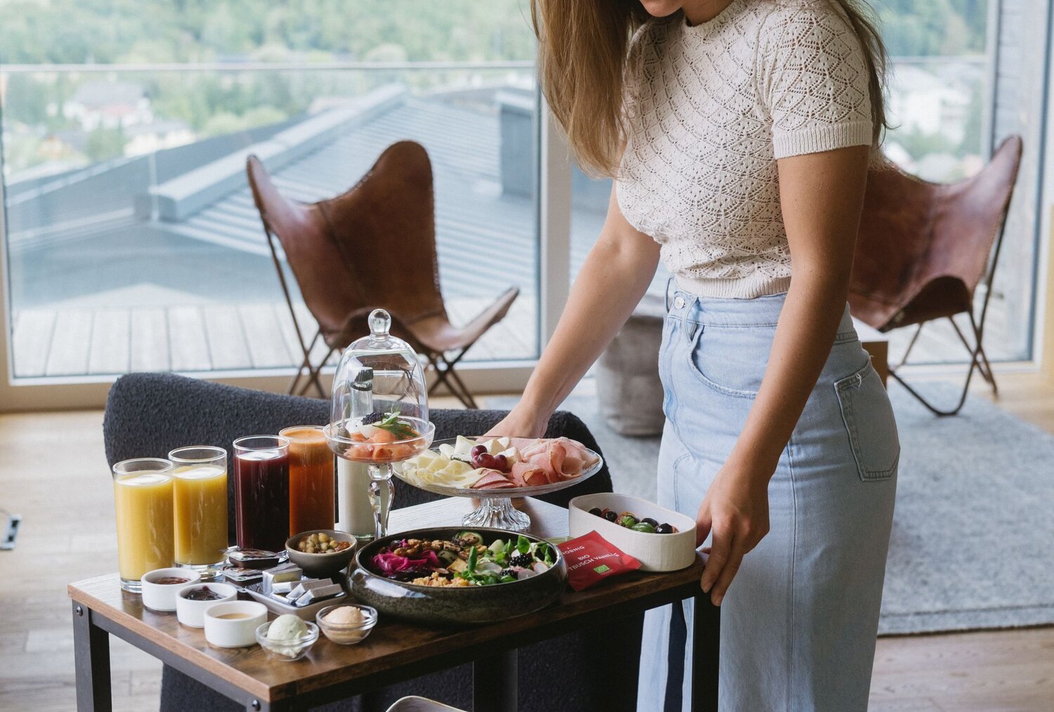 Woman arranging a breakfast cart with assorted dishes indoors.