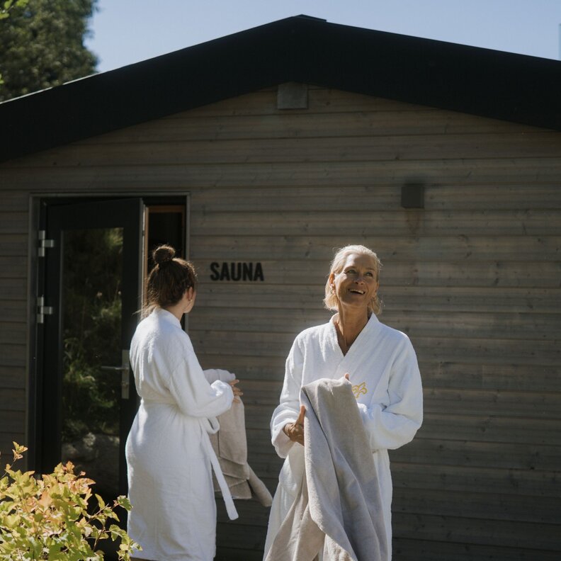 Zwei Frauen in Bademänteln mit Handtüchern vor einer Sauna